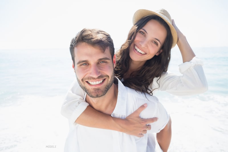 Man and woman smiling at the camera with the ocean in the background