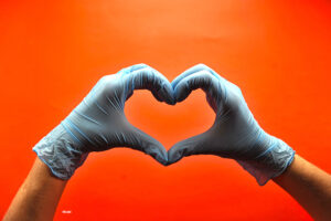 Two hands wearing surgical latex gloves form a heart against a red background.