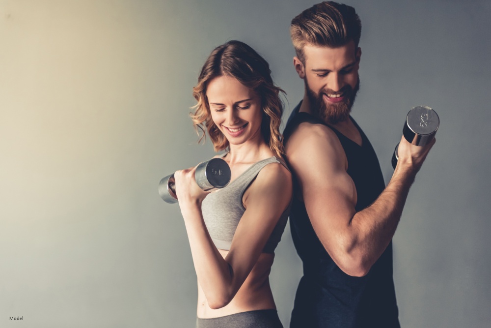 Young people are working out with dumbbells and smiling, on gray background